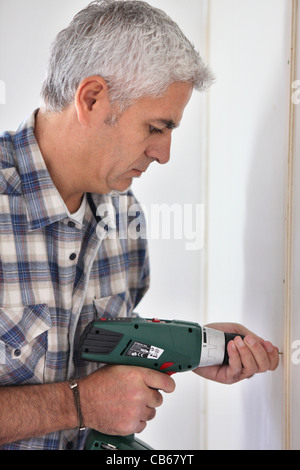 Grey- haired man drilling hole in wall Stock Photo