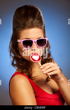Close-up portrait of beautiful woman licking lollipop and wearing pink glasses Stock Photo