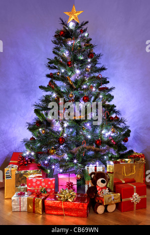 Photo of a Christmas tree with decorations and fairy lights surrounded by presents on a wooden floor Stock Photo