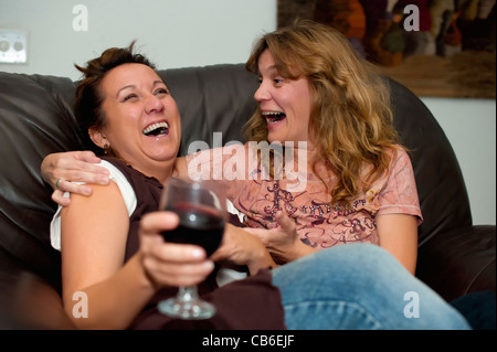 Two women enjoying wine, laughing and having fun while sitting on a sofa Stock Photo