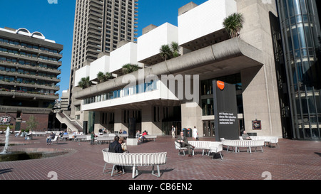 People sitting on benches in the sunshine outside the Barbican Centre entrance in the City of London England UK KATHY DEWITT Stock Photo
