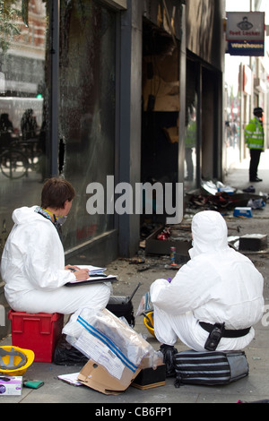 Police forensics search a burnt out Foot Locker sports wear store looted and set alight during rioting in Brixton, London. Stock Photo