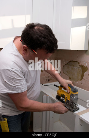 Tradesman using jigsaw tool to cut units for new kitchen installation in residential home, Bordon, Hampshire, UK. Stock Photo