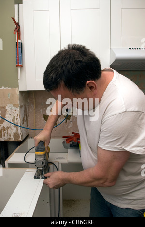 Tradesman using jigsaw tool to cut units for new kitchen installation in residential home, Bordon, Hampshire, UK. Stock Photo