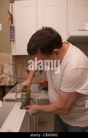 Tradesman using jigsaw tool to cut units for new kitchen installation in residential home, Bordon, Hampshire, UK. Stock Photo