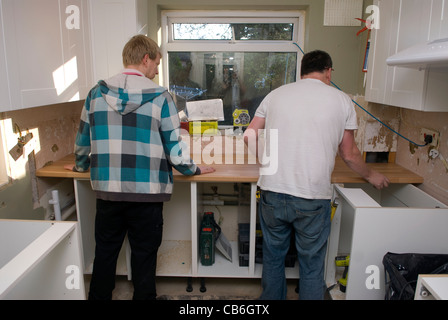 Tradesman (right) and his assistant positioning worktop in new kitchen installation in residential home, Bordon, Hampshire, UK. Stock Photo
