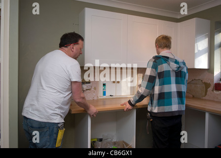 Tradesman (left) and his assistant positioning worktop in new kitchen installation in residential home, Bordon, Hampshire, UK. Stock Photo