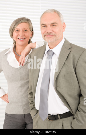 Professional elegant smiling senior businesswoman leaning against her male colleague Stock Photo
