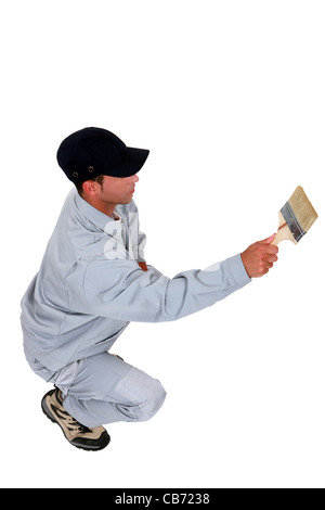 Squatting tradesman painting a wall Stock Photo