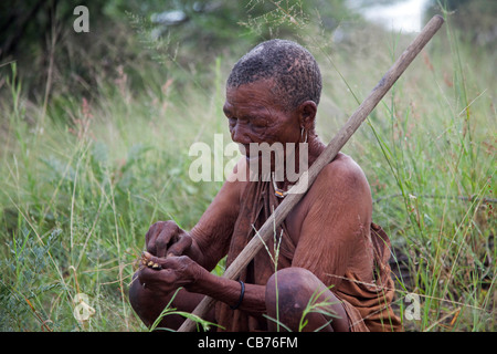 Elderly Bushman / San woman with roots for making paint pigment in the Kalahari desert near Ghanzi, Botswana, Africa Stock Photo