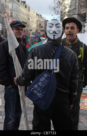 two men talk to male member of Anonymous anarchist hackivist political protest group, Occupy London, St Paul's Cathedral. Stock Photo