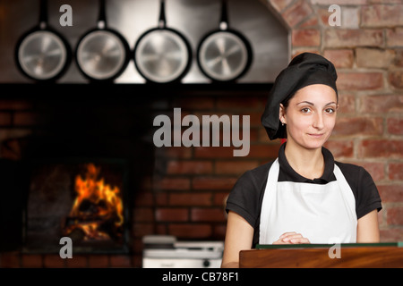 Woman Chef standing in the kitchen of her italian pizzeria restaurant in front of the wood oven Stock Photo