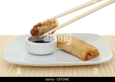 Chinese pancake roll dipping into soy sauce, with chopsticks, a ramekin and plate on a bamboo mat Stock Photo