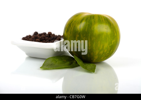 One green zebra organic tomato with basil leaves and a bowl with peppercorns isolated on white background Stock Photo