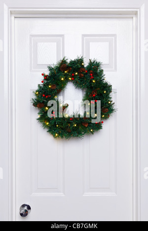Photo of a Christmas wreath with lights hanging on a white front door. Stock Photo
