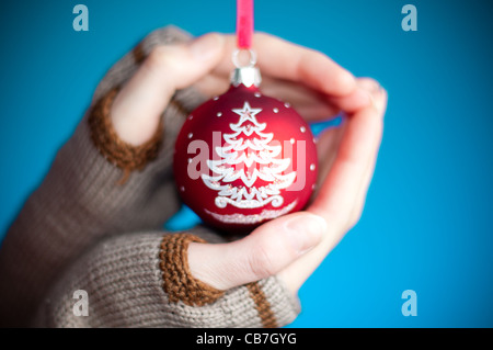 young woman's hands against blue background wearing winter clothes holding red christmas ball toy Stock Photo
