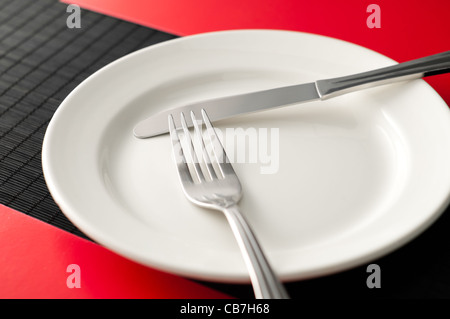 empty white plate on black table with knife and fork on the plate and red napkins by the sides of the plate Stock Photo
