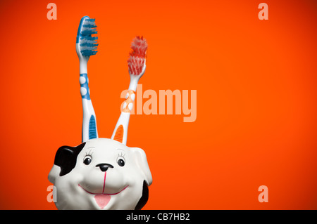 two toothbrushes in the glass resembling smiling dalmatian dog's head against orange background Stock Photo