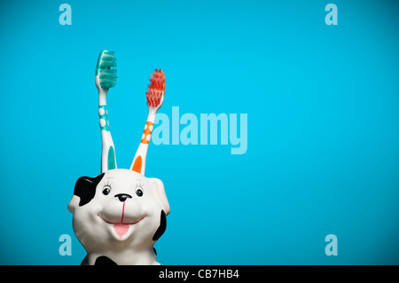 two toothbrushes in the glass resembling smiling dalmatian dog's head against blue background Stock Photo