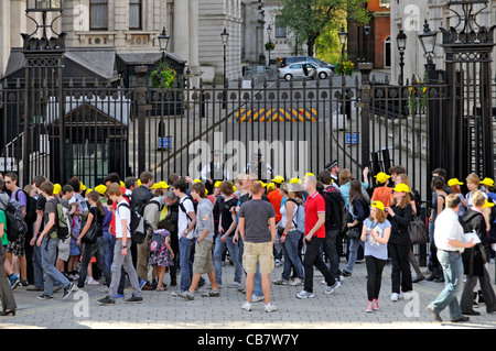 Armed London Metropolitan police officers behind security gate protect access to10 Downing Street tourists & group of school kids in caps Whitehall UK Stock Photo