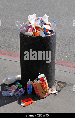 Waste management required to overflowing roadside litter bin full with rubbish garbage litter & trash spilling on pavement busy London street uk Stock Photo