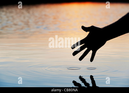 Hand touching water causing ripple at sunrise silhouette Stock Photo