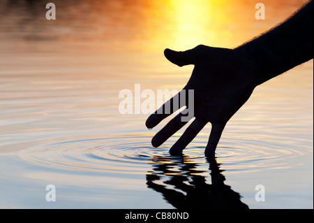 Hand touching water causing ripple at sunrise silhouette Stock Photo