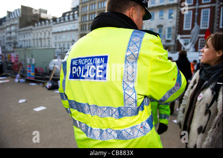 Rear view of Metropolitan police officer wearing high visibility jacket speaking to female member of the public. Stock Photo