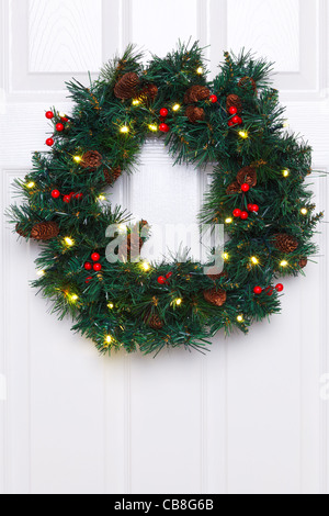 Photo of a Christmas wreath with fairy lights hanging on a white door. Stock Photo