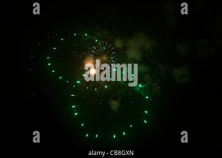 Three small sparse firework explosions barely light up the sky and a cloud of gunpowder hangs in the sky lit up by the firework Stock Photo