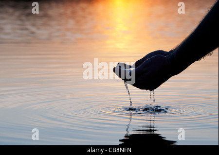 Cupped hands scooping up water in a still lake at sunrise in India. Silhouette Stock Photo