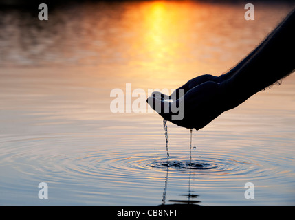 Cupped hands scooping up water in a still lake at sunrise in India. Silhouette Stock Photo