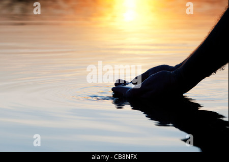 Cupped hands scooping up water in a still lake at sunrise in India. Silhouette Stock Photo