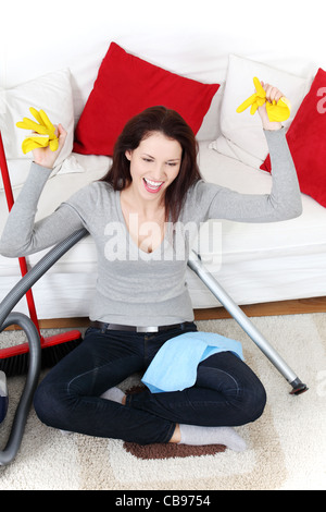 Front view of a full lenght young woman cleaning up at home, sitting on the floor next to the vacuum cleaner and a broom. Stock Photo