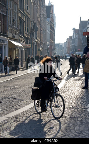 Woman cyclist on cobbled street (Steenstraat)  in Bruges town centre in winter, Bruges, Belgium.