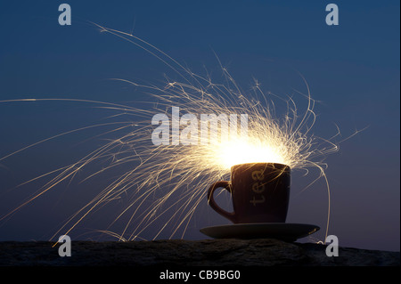 Fiery storm in a teacup concept. Fire cracker in a cup at night Stock Photo