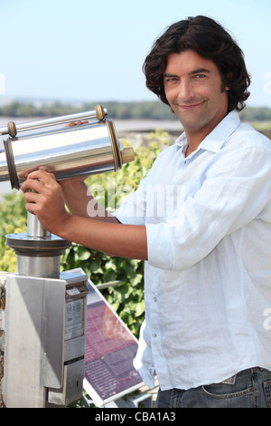 Man looking through a public telescope over an estuary Stock Photo