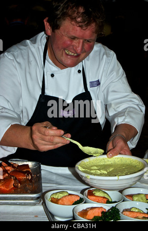 Catering chef spooning creme fraiche salsa verde sauce over serving bowl cooked salmon orzo broccoli Stock Photo