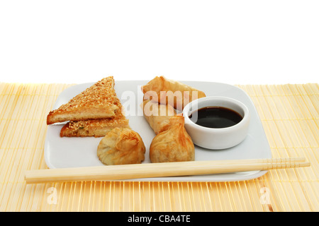 Selection of Chinese snacks on a plate with chopsticks and a ramekin of soy sauce on a bamboo matt Stock Photo