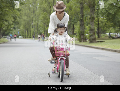 A girl riding a bicycle with training wheels Stock Photo