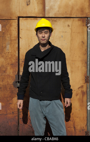 Chinese construction worker in front of a rusty entrance to a storage space. Stock Photo