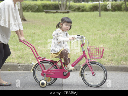 A girl riding a bicycle with training wheels Stock Photo