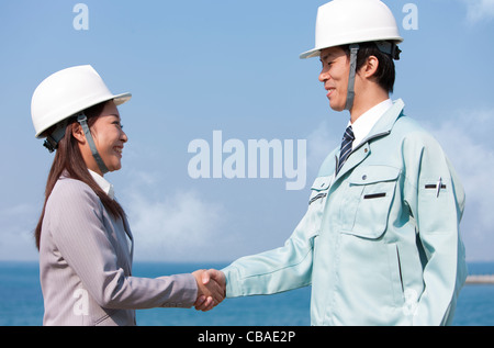 Two Businesspeople with Hardhats Shaking Hands Stock Photo