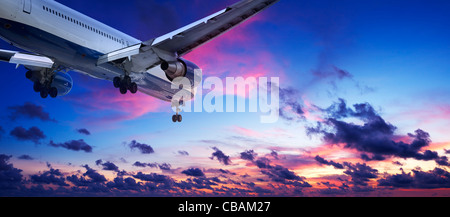 Jet aircraft is maneuvering for landing in a sunset sky. Panoramic composition. Stock Photo