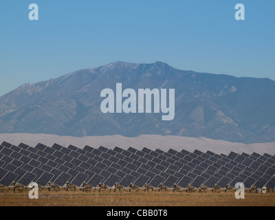 A series of large solar panels forms a symmetrical line at a power plant in the San Luis Valley of central Colorado. These panels utilize a tracking system to follow the sun, collecting its energy and using photovoltaic cells to transform the sunlight into electricity. Stock Photo