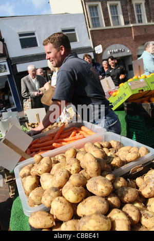 greengrocer on Doncaster Market in sunshine with new potatoes in foreground Stock Photo