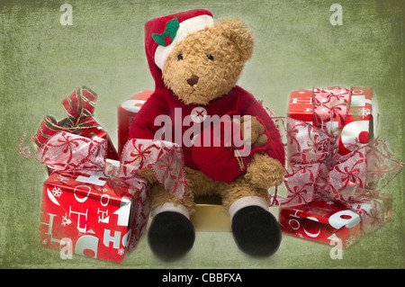 Teddy at Christmas. Well loved child's teddy dressed as Santa sitting among presents. Stock Photo