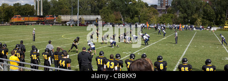 American high school football game being played outside with a Burlington Northern Santa Fe railroad train in the background Stock Photo