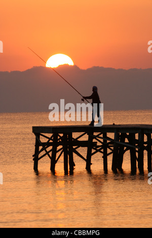 Fisherman at end of pier at sunrise Stock Photo
