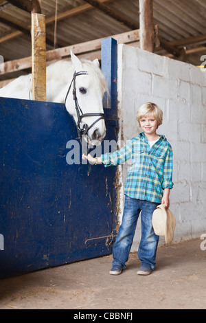 Boy standing with horse in stable Stock Photo